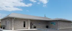 An image of a building with a gray roof and a blue sign that reads All Palm Eye Care, with potted plants in front of it